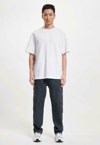 Witte katoenen t-shirt met een losse pasvorm, gecombineerd met donkergrijze cargobroek met meerdere zakken en een zachte textuur. Witte sneakers zorgen voor contrast.