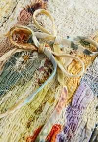 Deux liens en tissu noués en nœuds papillon sur une surface texturée matelassée multicolore avec des motifs cousus dans des tons terreux.