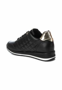 Zapatilla sintética negra con textura acolchada en los costados, acento metálico brillante en el talón y suela blanca a rayas. Cierre con cordones, cuello acolchado.