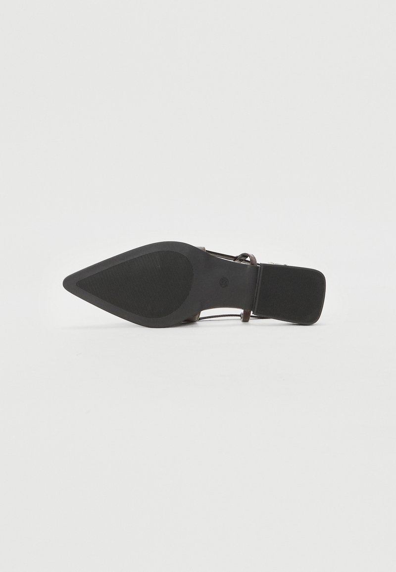 Chaussure noire à bout pointu avec une semelle en caoutchouc texturée, une fine bride et une boucle ajustable, présentant un design épuré et un matériel minimaliste.