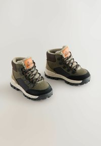 Bottes de randonnée avec un dessus vert et marron, doublure en fourrure, semelle en caoutchouc noir et lacets à motifs avec une étiquette d'accent marron.