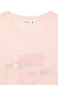 T-shirt in cotone rosa con scollatura rotonda. Presenta una grafica di un cuore metallizzato oro e dettagli morbidi a pennellate in rosa più chiaro. Etichetta del marchio visibile.