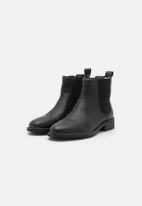 Botas Chelsea de cuero negro con paneles laterales elásticos, punta redondeada y un tacón bajo, con tiradores para facilitar su calzado.
