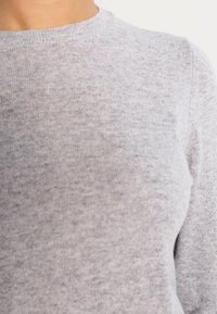 Ljusgrå stickad tröja med rund halsringning. Materialet verkar mjukt med en fin textur och visar subtila variationer i färg.