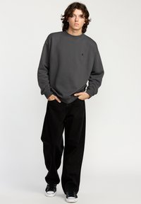 Gray sweatshirt with a crew neckline, black loose-fit jeans, and black sneakers. The sweatshirt features a small logo on the chest.