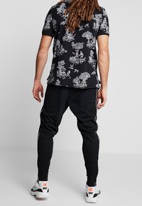 Zwarte short-sleeve shirt met wit bloemenpatroon, gecombineerd met zwarte tapered joggers met witte zijstrepen en witte sportschoenen.