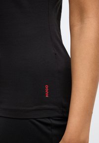 Black fitted tank top made of soft fabric, featuring a red "HUGO" logo on the left side and a sleek, minimalist design.