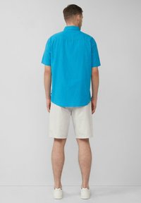 Kurzärmliges, leuchtend blaues Hemd aus Baumwolle mit Button-Down-Kragen, kombiniert mit hellgrauen, knielangen Shorts und weißen Turnschuhen.