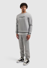 Grijze sweatshirt en bijpassende joggingbroek van zachte stof met een "BALLIN'" logo in het zwart. De outfit heeft een ontspannen pasvorm en elastische boorden.