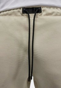 Beiga sweatpants med en mjuk textur och elastisk midja. Svarta dragsnoddar trätt genom en svart tygöglan.