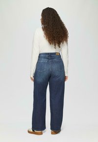 Donkerblauwe denim wide-leg jeans met een hoge taille, voorzien van twee achterzakken en een lichtbruine leren merklabel nabij de tailleband.