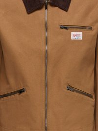Veste de travail marron avec fermeture éclair frontale, trois poches zippées, et col en velours côtelé foncé.