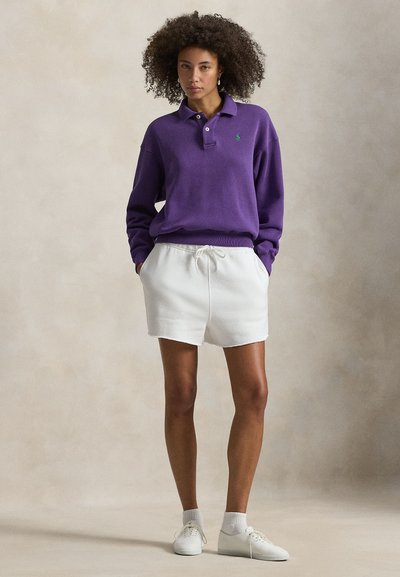 Μωβ πόλο μπλούζα με μακριά μανίκια και πράσινο λογότυπο, συνδυασμένη με λευκά σορτς με κορδόνι και λευκά αθλητικά παπούτσια. Υφή υφάσματος, άνετη εφαρμογή.