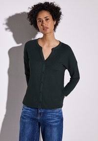 Mörkgrön långärmad topp med knäppning fram och rundad halsringning, kombinerad med ljusblå denim jeans. Texturerad tyg.