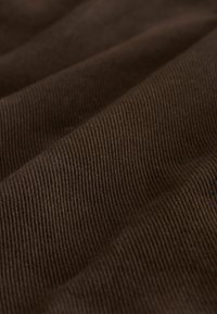 Close-up of dark brown corduroy fabric showing fine vertical ridges and soft, folded texture.