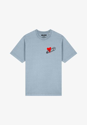 Ljust blå bomulls t-shirt med korta ärmar, med en svart säkerhetsnål och en röd hjärt-grafik på vänster bröst.