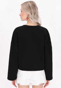 Felpa nera a maniche lunghe con un neckline arrotondato, abbinata a pantaloni corti bianchi strappati. Presenta una texture liscia.