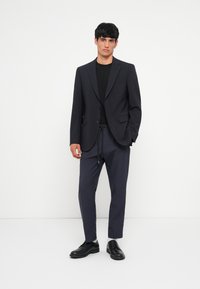Námornícky oblek s dvojitým gombíkom, skombinovaný s čiernym tričkom a námorníckymi nohavicami so šnúrkou. Čierne topánky dotvárajú outfit.