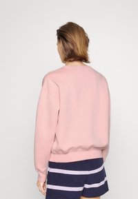 Sweatshirt rose avec encolure et poignets côtelés, présentant une coupe décontractée. Porté avec un short à rayures bleu marine et blanches.