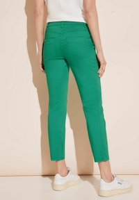 Gröna bomullsbukser med slim fit, två bakfickor och en nederkant strax över vristen, i kombination med vita sneakers.