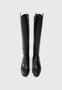 Un par de botas altas de cuero negro con cremalleras laterales, punteras puntiagudas y tiradores en la parte superior sobre un fondo claro.