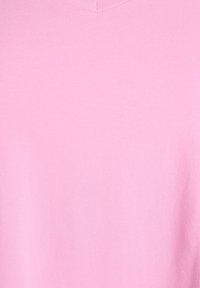 Ružičasta majica s V izrezom napravljena od mekane, glatke tkanine. Jednostavan dizajn s uniformnom teksturom, bez vidljivih uzoraka ili akcenta.