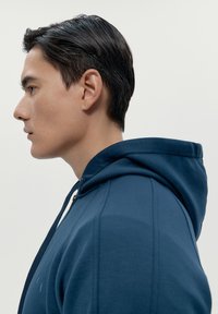 Felpa con zip di colore blu navy, con una finitura testurizzata, dotata di cappuccio foderato e lacci, cuciture visibili e un design aderente.