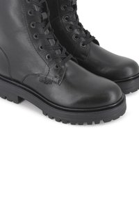 Botas de combate negras de cuero con superficie texturizada, diseño con cordones, suela de goma resistente y patrón de banda de rodadura prominente.