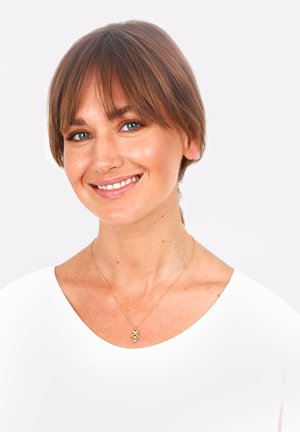 Goldene Halskette mit einem Anhänger, getragen von einer Person mit kurzen Haaren und einem weißen Oberteil vor einem neutralen Hintergrund.
