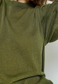 Grön stickad tröja med skimrande textur, rund urringning och puffärmar, med en avslappnad passform och vävt mönster.