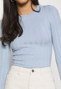 Haut à manches longues côtelé bleu clair avec un col rond, associé à un pantalon taille haute de couleur crème avec un détail de bouton en métal.