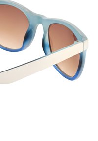 Niebieskie gradientowe okulary przeciwsłoneczne w dużym kocim kształcie. Przezroczysta plastikowa oprawka z białymi zausznikami i przyciemnionymi brązowymi szkłami.