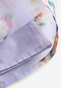 Zbliżenie na złożoną jasnofioletową tkaninę z częściowo widoczną pod spodem tkaniną w kwiatowy wzór, z widocznymi zszytymi krawędziami.