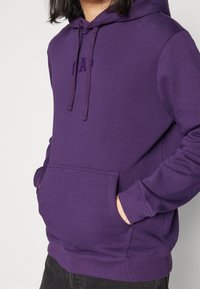 Sudadera morada con bolsillo delantero y capucha con cordón. Confeccionada en una mezcla de algodón, presenta un logo sutil en el pecho y puños acanalados.