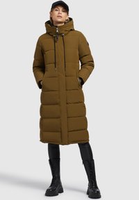 Long olive green puffer coat with a hood, featuring a front zipper, side pockets, and adjustable drawstrings. Textured panels throughout.