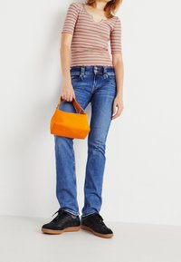 Randig, figurnära topp med kort ärm i röd och vit, tillsammans med blå denimjeans. Orange handväska; svarta sneakers med gummisålar.