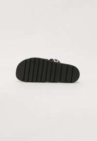 Flache schwarze Sandalen-Sohle mit strukturierten Rillen, die eine glatte, abgerundete Zehenpartie und eine erhöhte Ferse aufweist. Hergestellt aus einem gummiähnlichen Material.