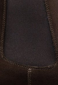 Bottine en suède marron avec panneaux latéraux élastiques, présentant une texture lisse et des coutures contrastantes autour des bords.