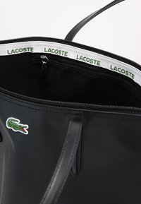 Borsa tote nera in nylon, con chiusura a zip, tasca in rete all'interno e rifiniture verde e bianco con logo di coccodrillo.