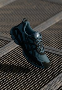 Chaussure de sport en teal et noir avec une tige en textile mesh, semelle texturée, col rembourré et éléments de design contrastants.