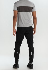 Camisa de hombre gris y negra de manga corta con rayas horizontales, combinada con pantalones negros con detalles reflectantes y piernas ajustadas.