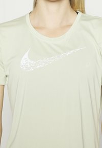 Camiseta de Nike de color verde claro con un diseño de logo swoosh blanco en el pecho, mangas cortas y cuello redondo. Textura de tela suave.