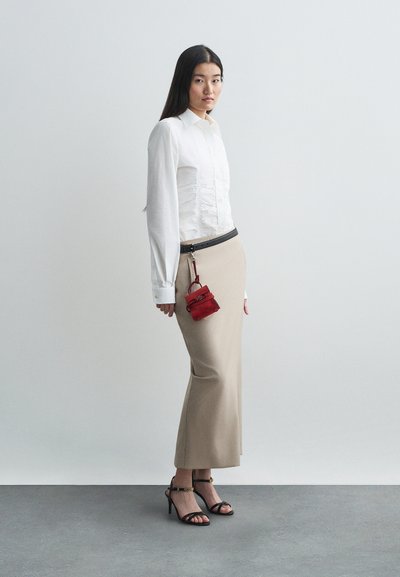 Λευκή πουκαμίσα με μακριά μανίκια και φουσκωτά, μπεζ μολυβένια φούστα, μαύρη ζώνη, κόκκινη μίνι τσάντα και μαύρες ψηλοτάκουνες σандάλια με λουράκια.