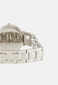 Ασημί ρολόι από ανοξείδωτο ατσάλι με στρογγυλή κάσα, αλυσίδα συνδέσμου, λεία επιφάνεια και χαραγμένες λεπτομέρειες στο πίσω μέρος. Διαθέτει στρογγυλές ασημένιες λεπτομέρειες.