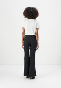 Black flared pants with white side stripes paired with a white short-sleeve top. The design features a fitted waist and subtle branding on the top.