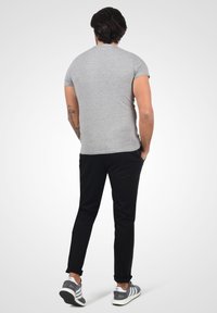 Grijze katoenen t-shirt met korte mouwen, gecombineerd met zwarte slim-fit broek en grijze sneakers met witte en zwarte strepen.