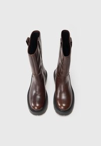 Botas de cuero marrón hasta el tobillo con un acabado suave, puntera redondeada, paneles laterales elásticos y suelas de goma para mayor durabilidad.