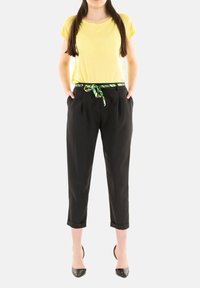 T-shirt giallo a maniche corte abbinato a pantaloni neri con una cintura verde a righe e scarpe con tacco nere. Texture lisce.