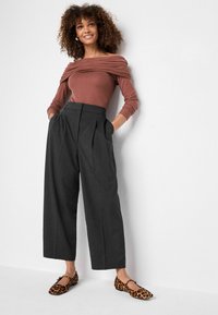 Top marrone senza spalline, pantaloni a vita alta grigi a righe sottili e larghi, e ballerine con stampa leopardata, con vestibilità rilassata e dettagli plissettati.
