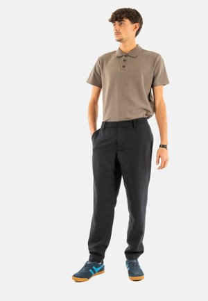 Polo de manga corta en color topo con un patrón texturizado, con una tapeta de tres botones. Pantalones negros a medida y zapatillas con acentos azules.